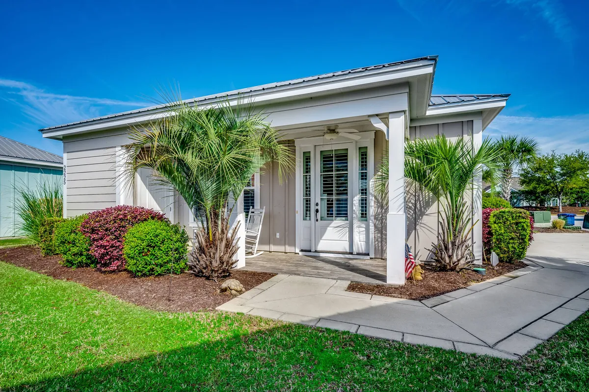 The hero image shows the charming front entrance of a single-family house framed by swaying palm trees, vibrant shrubs, and a welcoming pathway. The inviting porch hints at leisurely mornings and relaxing evenings.