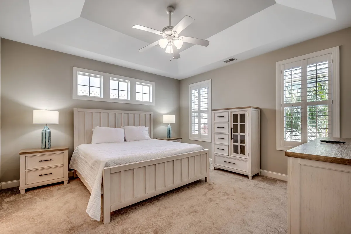 A tranquil bedroom featuring a neatly made bed with gentle coastal accents, flanked by nightstands and a dresser. Soft natural light filters through the windows, creating a restful and inviting atmosphere ideal for unwinding.