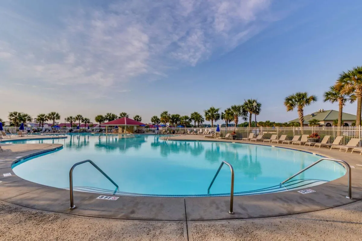 This exterior image features a swimming pool flanked by palm trees and lined with lounge chairs under an open blue sky. The tranquil setting suggests a leisurely pace and encourages guests to unwind and socialize in a relaxed outdoor environment.