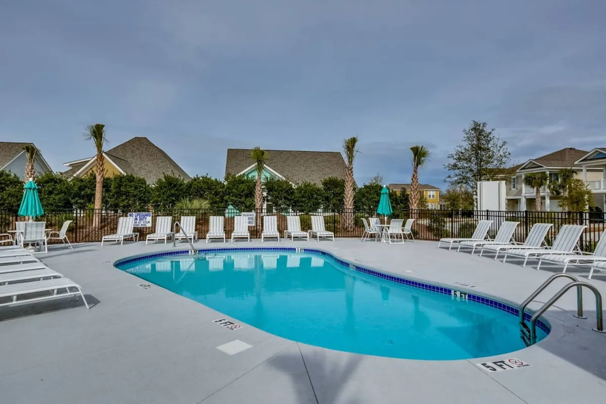 This image captures a sparkling swimming pool bordered by inviting lounge chairs, swaying palm trees, and shaded umbrellas. The pool area is sunlit, evoking a resort-like atmosphere perfect for both relaxation and social gatherings.